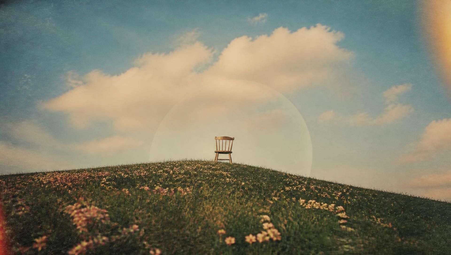 An empty chair on a flowered hill beneath an immense sky